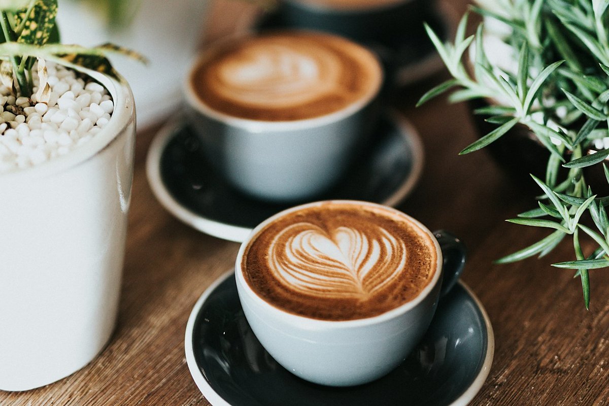 Two latte-art coffees on a wooden table with herbs